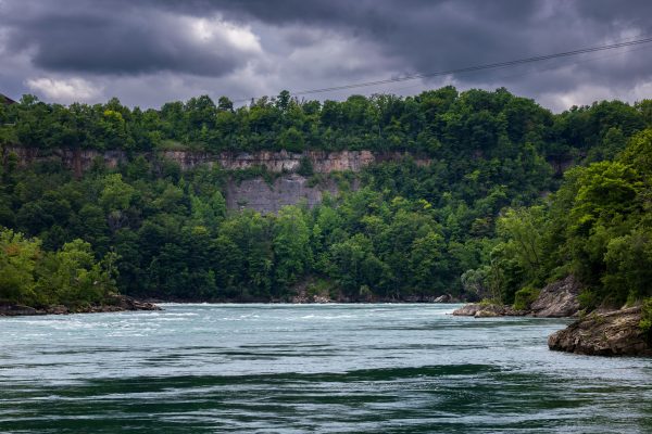 Expansive view of a river lined by dense forests under a dramatic cloudy sky. Nature 4K
