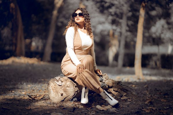 Fashionable woman seated on tree trunk in autumn forest, India Charme 4K
