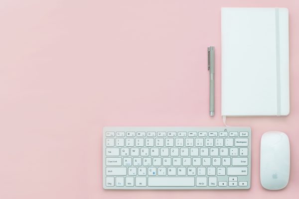 Flat lay of a minimalist workspace featuring a keyboard, notebook, and pen on a pink surface. Minimaliste 4K