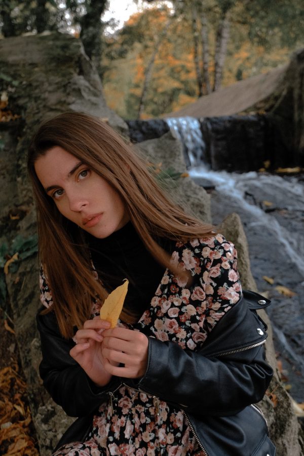 From above of young concentrated female in trendy wear with yellow leaf looking at camera near cascade in woods Mobile 4K