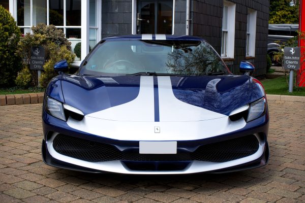 Front view of a Ferrari 296 GTB supercar with blue and white livery, parked in an urban setting. Voitures 4K