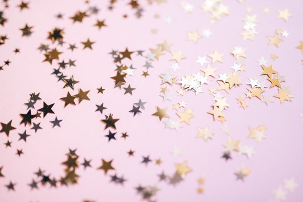 Gold and silver star confetti spread across a pastel pink surface, creating a festive and whimsical effect. Espace 4K
