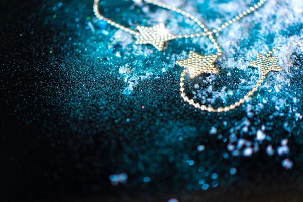 Golden star garland on a shimmering blue surface with scattered snowflakes, creating a festive mood. Espace 4K