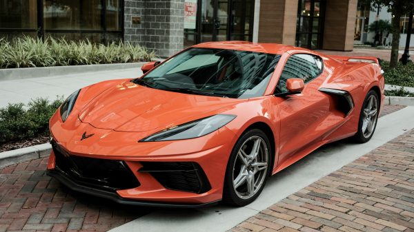 High-quality image of a shiny orange Corvette sports car parked on a brick road. Voitures 4K