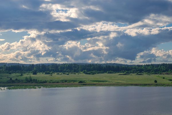 Idyllic Nordic countryside with lush fields and dramatic clouds over a tranquil river. Nature 4K