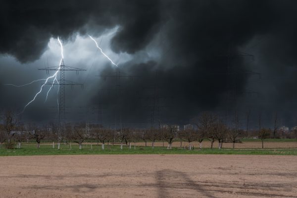 Intense lightning strikes during a storm over a countryside landscape with power lines. Dark 4K
