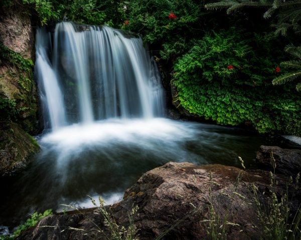 Long exposure fantastic scenery of rapid cascade flowing from rough cliff into small lake in abundant forest Nature 4K