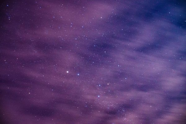 Long exposure of cosmic background with dark night sky with glowing bright stars behind light floating clouds Espace 4K