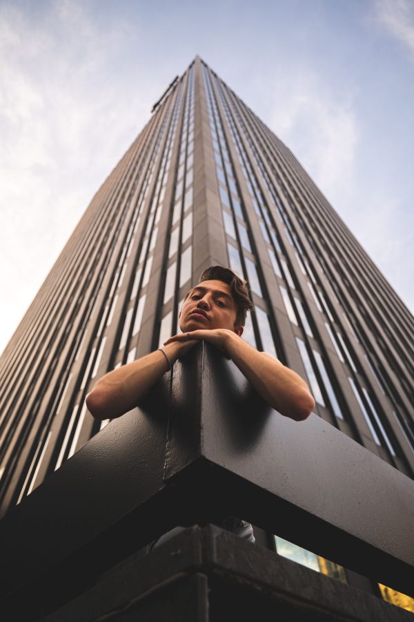 Low-angle portrait of a man posing against a towering skyscraper in a cityscape. Mobile 4K