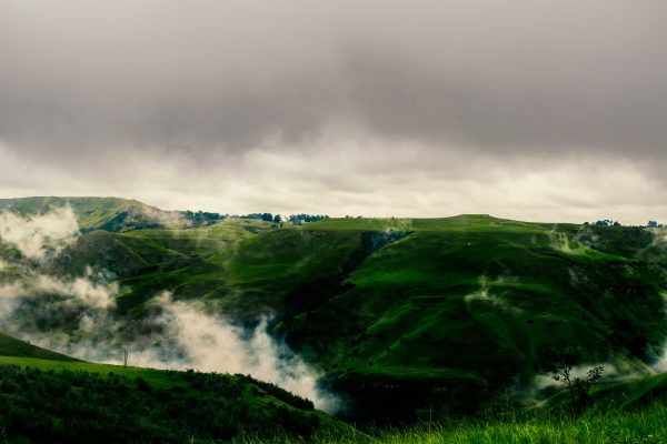 Lush green hills shrouded in mist beneath a cloudy sky, depicting tranquil nature. Nature 4K