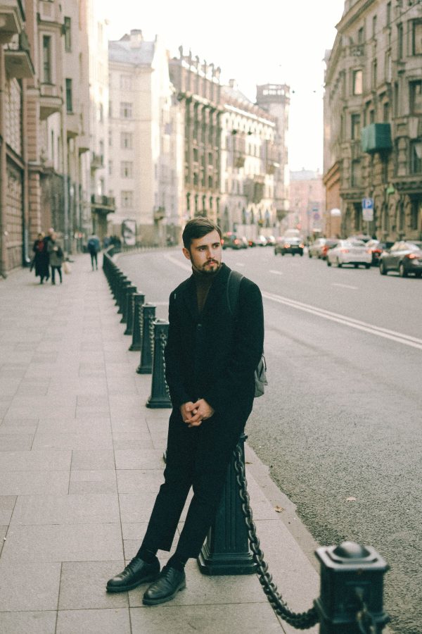 Man in black coat on city sidewalk with townhouse backdrop. Mobile 4K