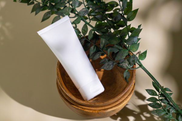 Minimalist skincare tube with green leaves in a wooden bowl, ideal for eco-friendly cosmetic themes. Minimaliste 4K
