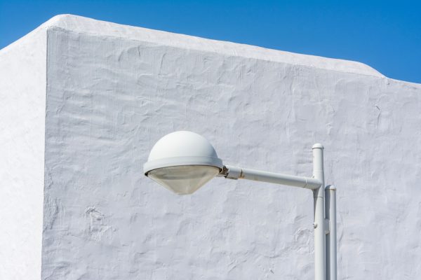 Minimalist white street lamp set against a textured white wall under a clear blue sky. Minimaliste 4K