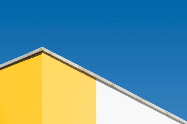 Modern building facade with yellow and white walls under a clear blue sky. Minimaliste 4K