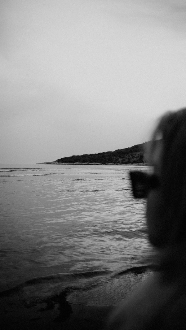 Monochrome view of coastline with silhouette of a person wearing sunglasses. Mobile 4K