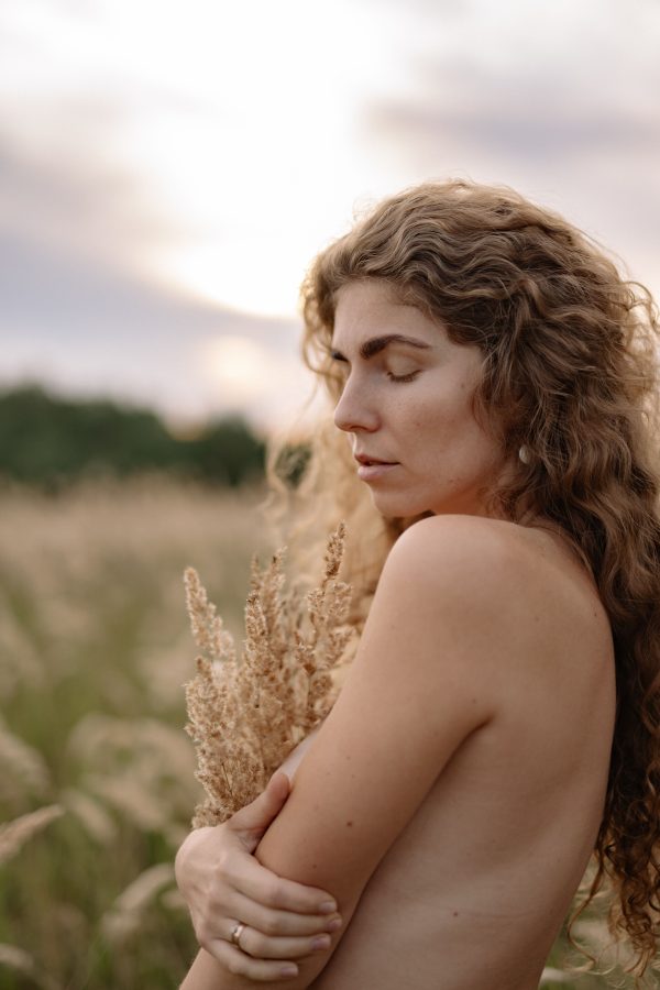 Peaceful portrait of a woman with wavy hair in a meadow at sunset, embracing nature. Mobile 4K