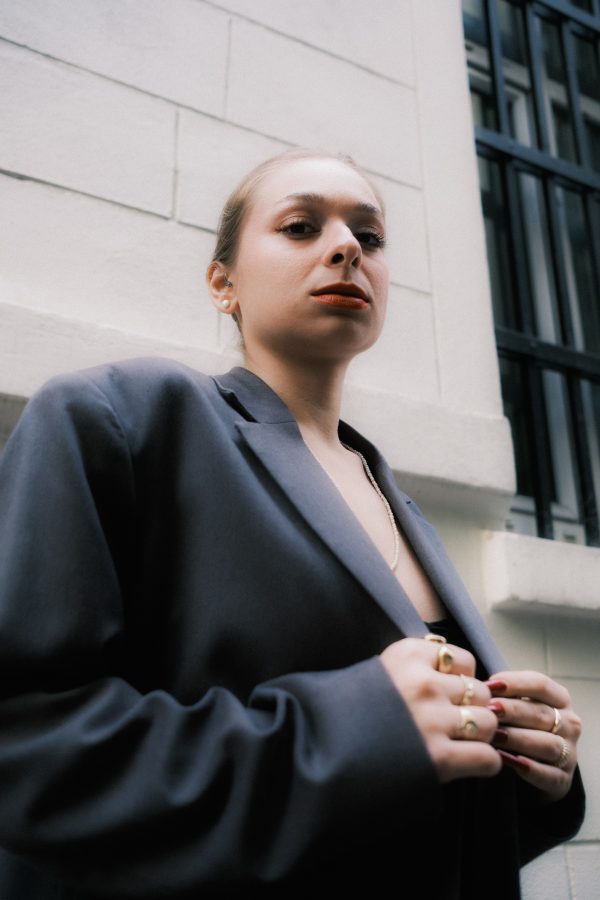 Portrait of a confident woman in an oversized blazer standing near a modern building exterior. Mobile 4K