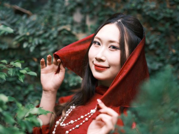 Portrait of a smiling woman in red Vietnamese ao dai amidst lush greenery outdoors. Charme 4K