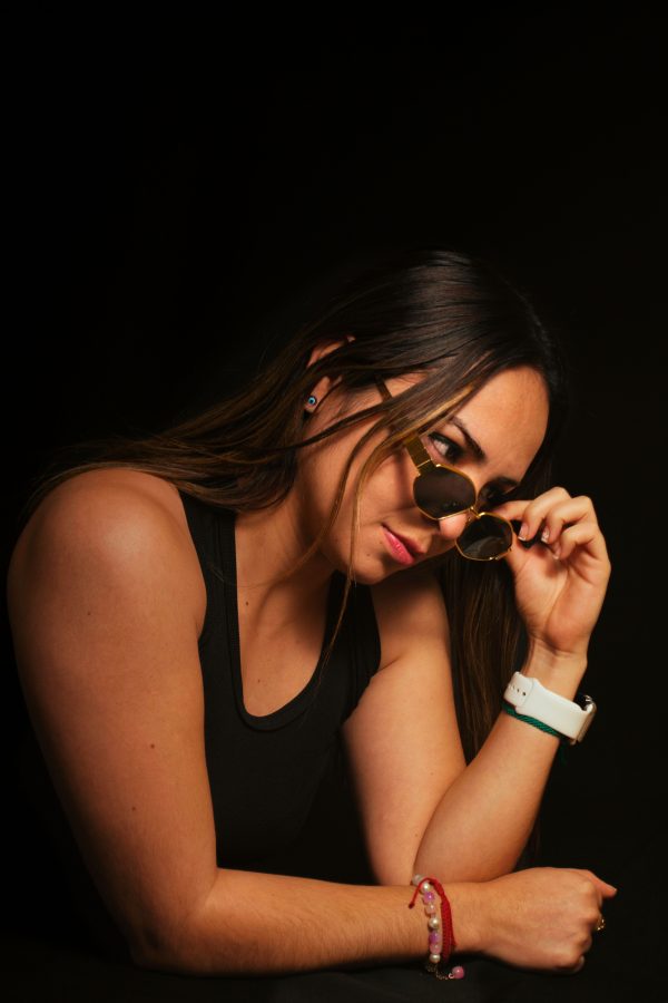 Portrait of a stylish woman wearing sunglasses in a dimly lit studio setting. Mobile 4K