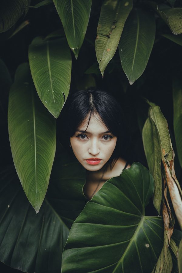 Portrait of a woman surrounded by lush green foliage, creating a mysterious look. Mobile 4K