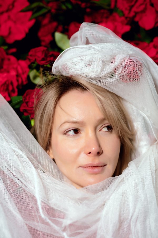 Portrait of a woman wrapped in white fabric with vibrant red flowers in the background. Mobile 4K