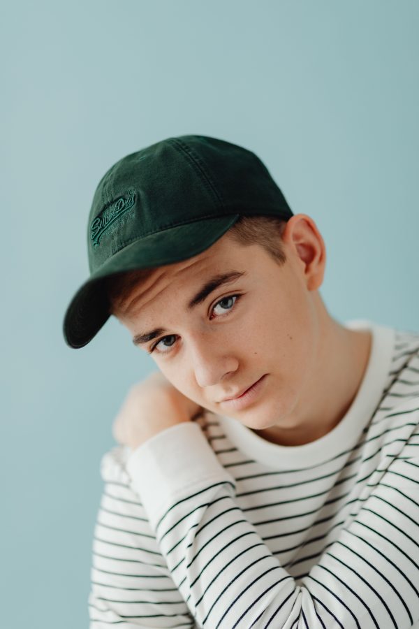 Portrait of a young man in a striped shirt and cap against a blue background. Mobile 4K