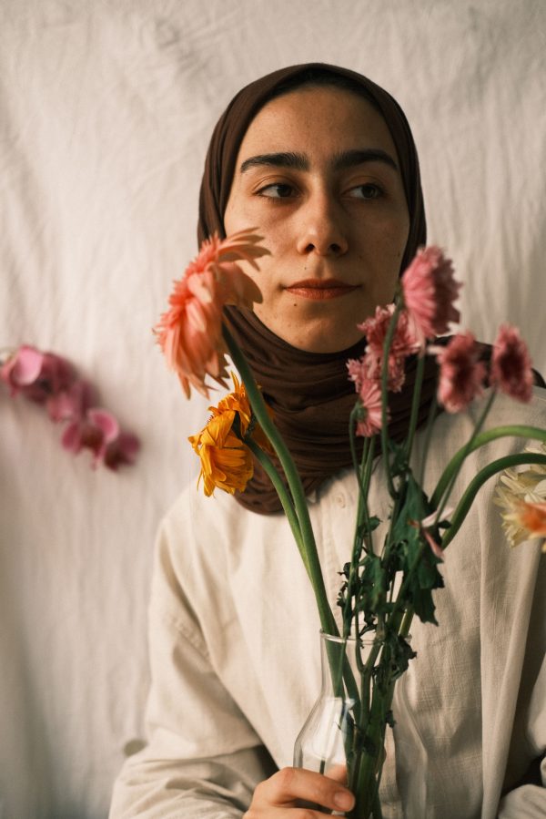 Portrait of a young woman in a hijab holding colorful flowers indoors with soft lighting. Mobile 4K