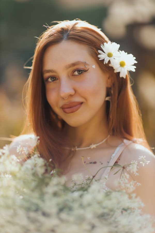 Portrait of a young woman with daisies in her hair, smiling in a sunlit garden. Mobile 4K