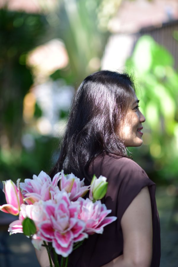 Profile of a woman holding pink lilies in a sunlit garden setting, exuding a serene mood. Mobile 4K