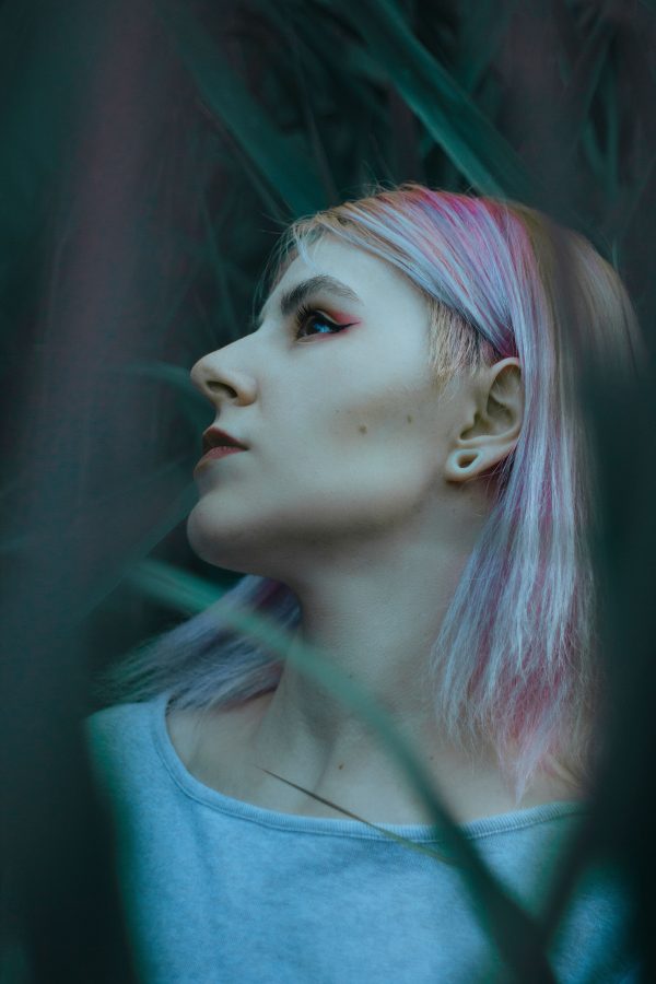 Profile portrait of a woman with pastel-dyed hair surrounded by green foliage. Mobile 4K