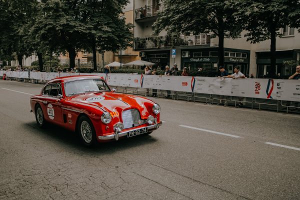 Red classic car participates in vintage racing event with spectators on urban street. Voitures 4K