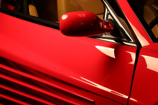 Red Ferrari Testarossa side mirror detail shot showcasing luxury design elements. Voitures 4K