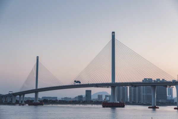 Scenic view of a modern cable-stayed bridge over water at twilight with city skyline in the background. Architecture 4K