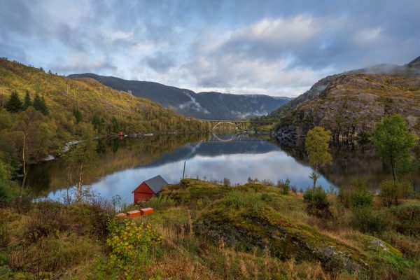 Scenic view of a tranquil lake reflecting mountains and a bridge in Norway. Nature 4K