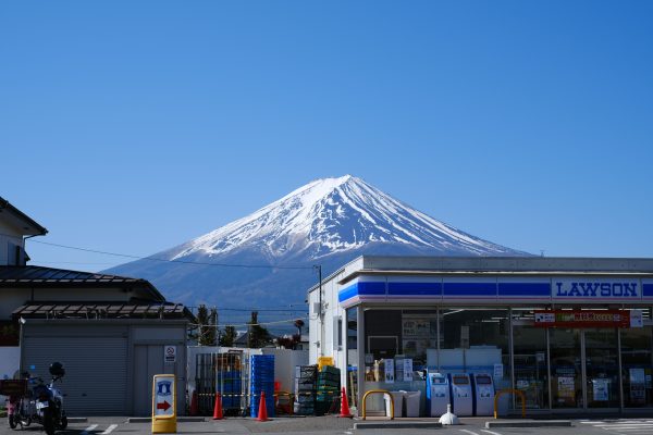 Scenic view of Mount Fuji behind a convenience store under a clear blue sky. Anime 4K