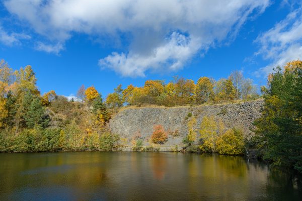Serene autumn landscape with a lake, trees, and vibrant foliage under a bright blue sky. Abstrait 4K