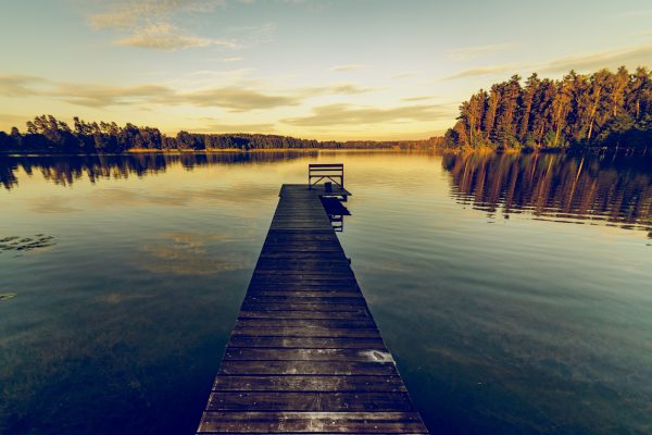Serene landscape of a wooden jetty over a calm lake at sunset, reflecting trees and sky. Nature 4K