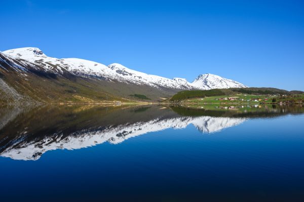 Serene landscape of snowy mountains reflecting on a calm lake in Eidsdal, Norway. Nature 4K