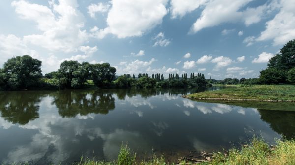 Serene river landscape with mirrored trees and cloudy sky in Höxter, Germany. Nature 4K