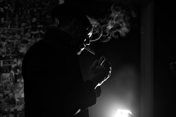 Silhouette of a mysterious man smoking with dramatic lighting in black and white. Dark 4K