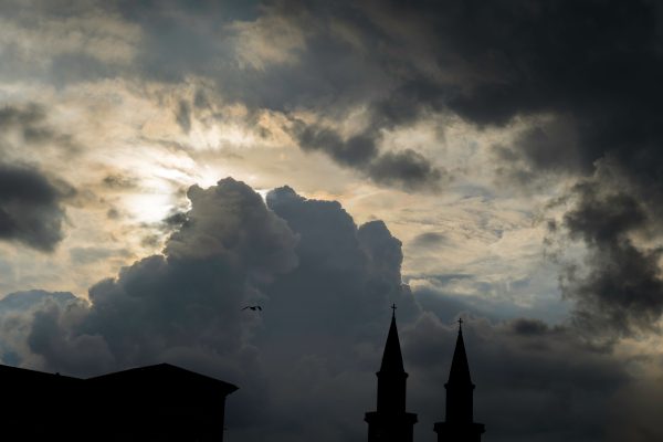 Silhouetted church towers beneath a dramatic sky filled with dark clouds and a hint of sunlight. Dark 4K