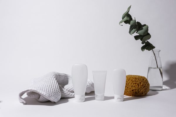 Simple and clean spa arrangement with white bottles, towel, and eucalyptus in vase. Minimaliste 4K