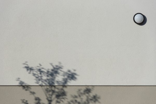 Simple exterior wall with a tree shadow and round light fixture creating a minimalist scene. Minimaliste 4K