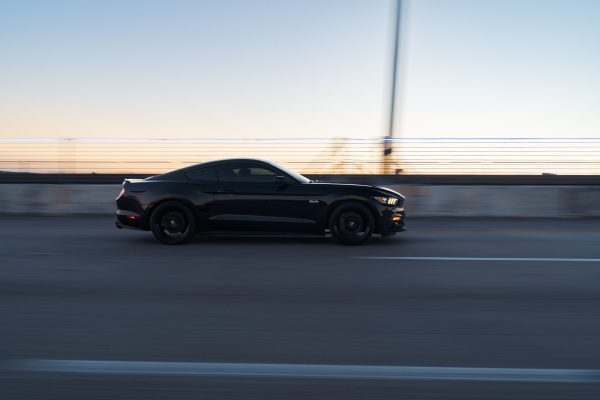 Sleek black car speeding on a highway at dusk, capturing motion and speed on a bridge. Voitures 4K