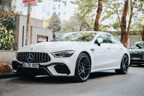 Sleek white luxury sedan parked on a tree-lined city street on a sunny day. Voitures 4K