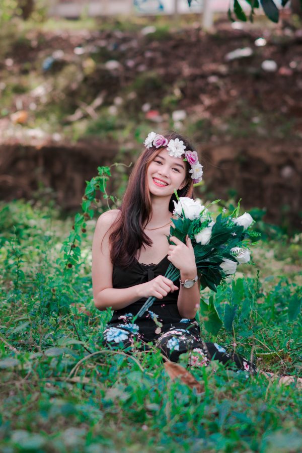 Smiling young woman with floral headdress holding bouquet in grassy field. Mobile 4K