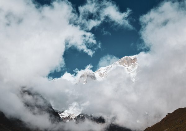 Snow-covered mountain peaks emerging through fluffy clouds under a clear blue sky. Nature 4K
