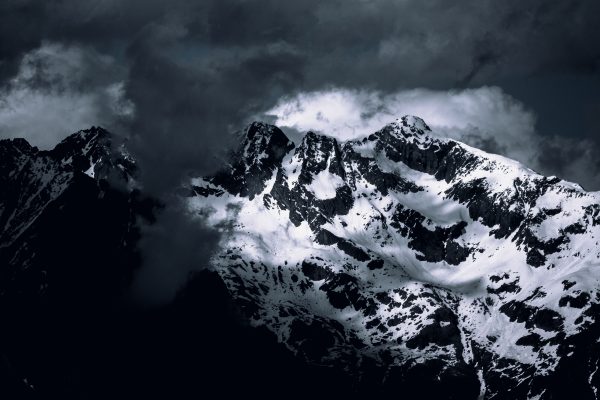 Snowcapped peaks of majestic mountains enveloped by dramatic clouds, showcasing winter's allure. Nature 4K