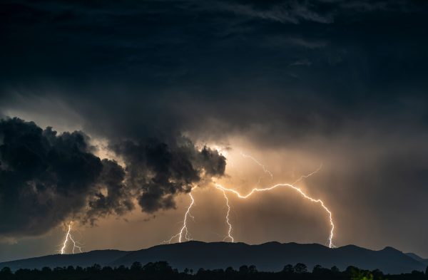 Spectacular lightning strikes illuminate dark clouds over a mountain range during a thunderstorm. Dark 4K