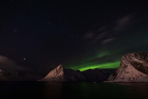 Spectacular view of the Northern Lights illuminating snowy peaks under a starlit sky. Espace 4K
